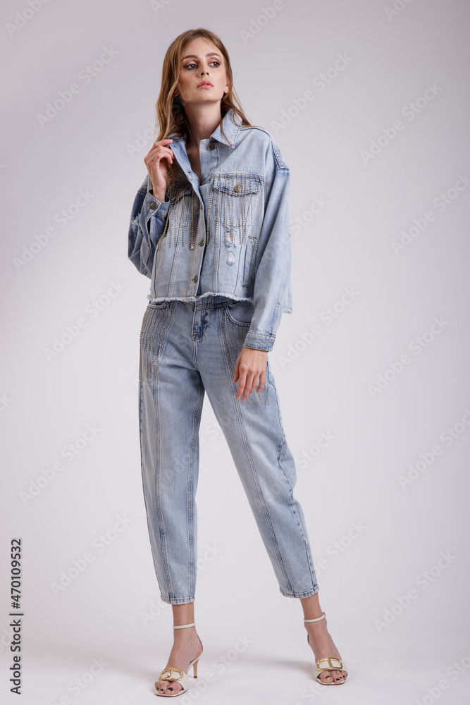 High fashion photo of a beautiful elegant young woman in a pretty denim jeans oversize jacket with rhinestones, pants posing over white, soft gray background. Slim figure. Studio Shot. High fashion photo of a beautiful elegant young woman in a pretty denim jeans oversize jacket with rhinestones, pants posing over white, soft gray background. Slim figure. Studio Shot.