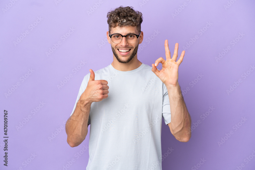 Fototapeta premium Delivery caucasian man isolated on purple background showing ok sign and thumb up gesture