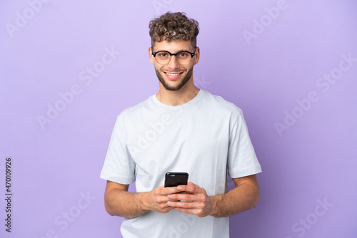 Delivery caucasian man isolated on purple background sending a message with the mobile