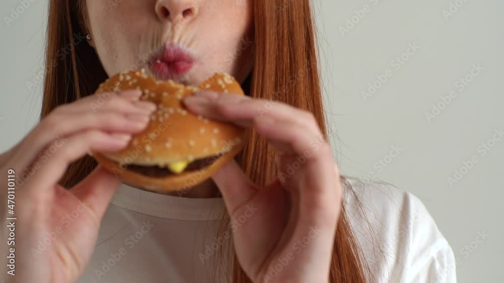 Close-up cropped shot face of unrecognizable young woman with enjoying to eat tasty burger on white isolated background in studio. Closeup front view of pretty female eating delicious hamburger. Close-up cropped shot face of unrecognizable young woman with enjoying to eat tasty burger on white isolated background in studio. Closeup front view of pretty female eating delicious hamburger.