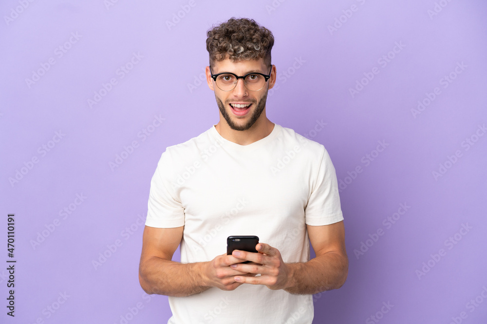 Delivery caucasian man isolated on purple background surprised and sending a message Delivery caucasian man isolated on purple background surprised and sending a message