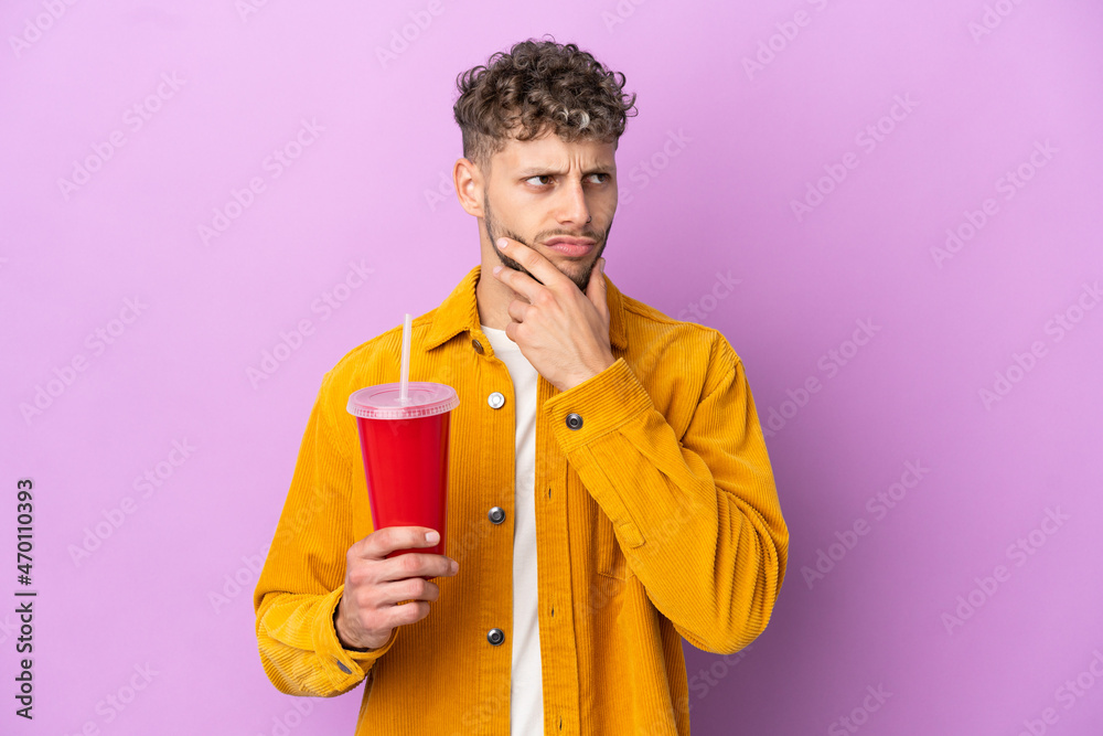 Young blonde man holding soda isolated on purple background having doubts Young blonde man holding soda isolated on purple background having doubts
