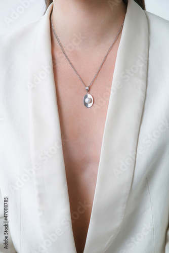 Trending silver necklace with pearls on a beautiful young girl in a white fashionable jacket. Beauty and fashion 
