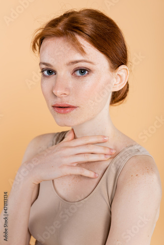 Canvastavla Portrait of young woman with freckled skin looking at camera isolated on beige