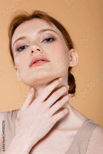 Portrait of redhead woman touching neck isolated on beige