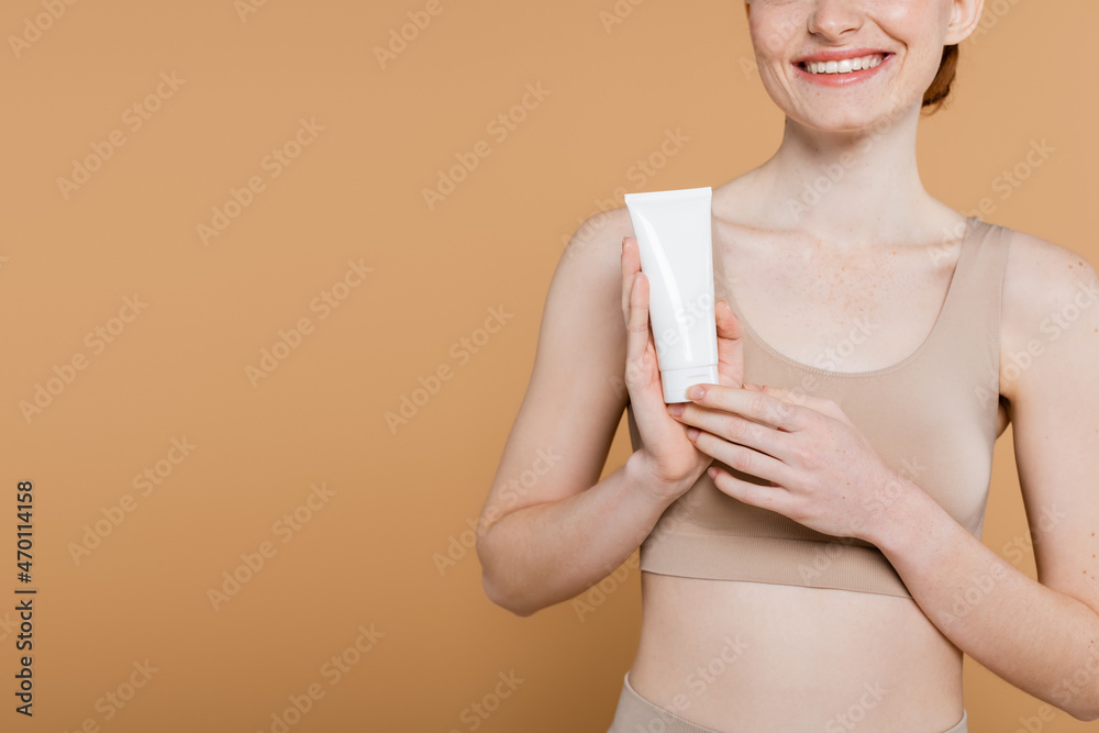 Cropped view of smiling woman in top holding tube with cosmetic cream isolated on beige Cropped view of smiling woman in top holding tube with cosmetic cream isolated on beige