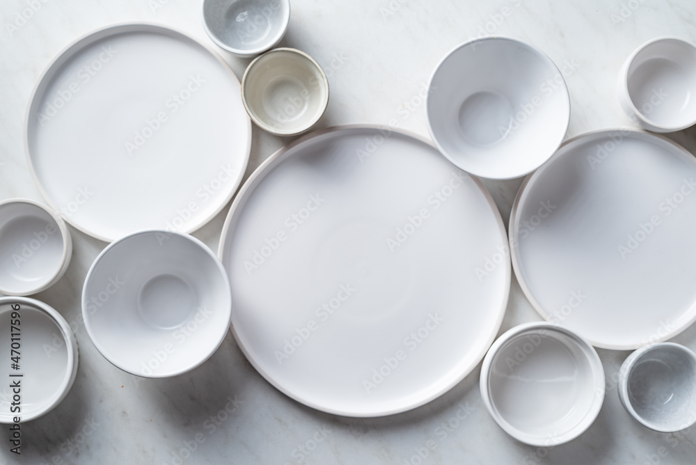 Empty white plates and bowls on white kitchen table. Overhead view. Empty white plates and bowls on white kitchen table. Overhead view.