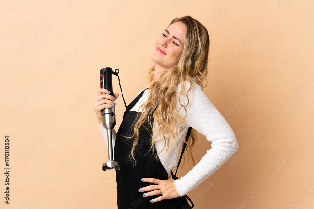 Young brazilian woman using hand blender isolated on beige background suffering from backache for having made an effort Young brazilian woman using hand blender isolated on beige background suffering from backache for having made an effort