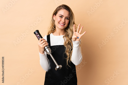Young brazilian woman using hand blender isolated on beige background happy and counting four with fingers