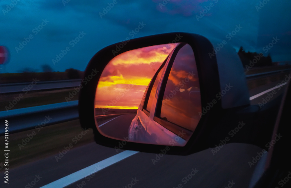 Nubes de atardecer reflejadas en el espejo retrovisor de un choche por la autopista