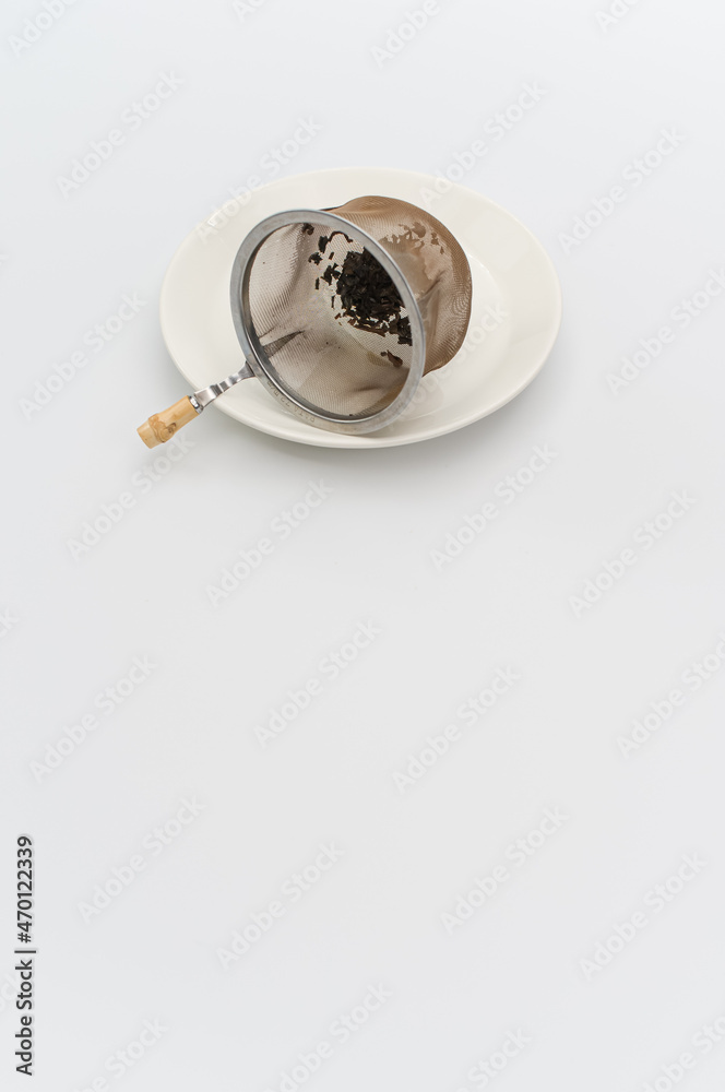 metal tea strainer with tea leaves on a white stoneware plate
