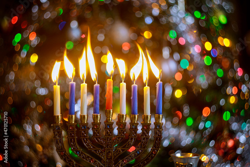 Burning candles on menorah for Hanukkah on defocus color lights background.