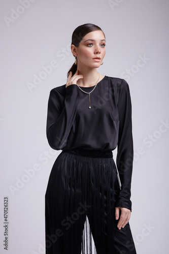 High fashion photo of a beautiful elegant young woman in a pretty black blouse, fringe trousers, accessories over white background. Studio Shot. Gathered dark hair. Slim figure