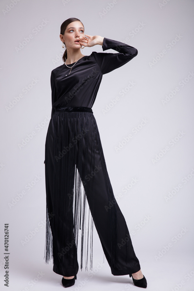 High fashion photo of a beautiful elegant young woman in a pretty black blouse, fringe trousers, accessories over white background. Studio Shot. Gathered dark hair. Slim figure High fashion photo of a beautiful elegant young woman in a pretty black blouse, fringe trousers, accessories over white background. Studio Shot. Gathered dark hair. Slim figure