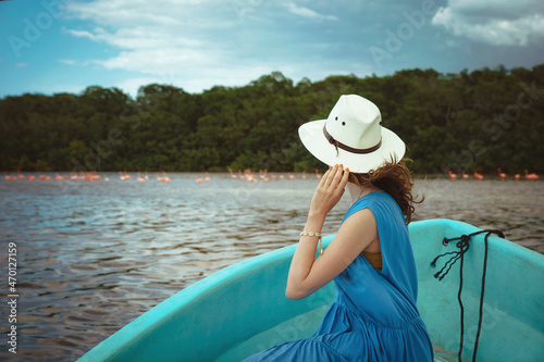 A young woman tourist in a boat watches pink flamingos in the Celestun National Park in Mexico. Flamingo birds at Ria Celestun Biosphere Reserve, Mexico