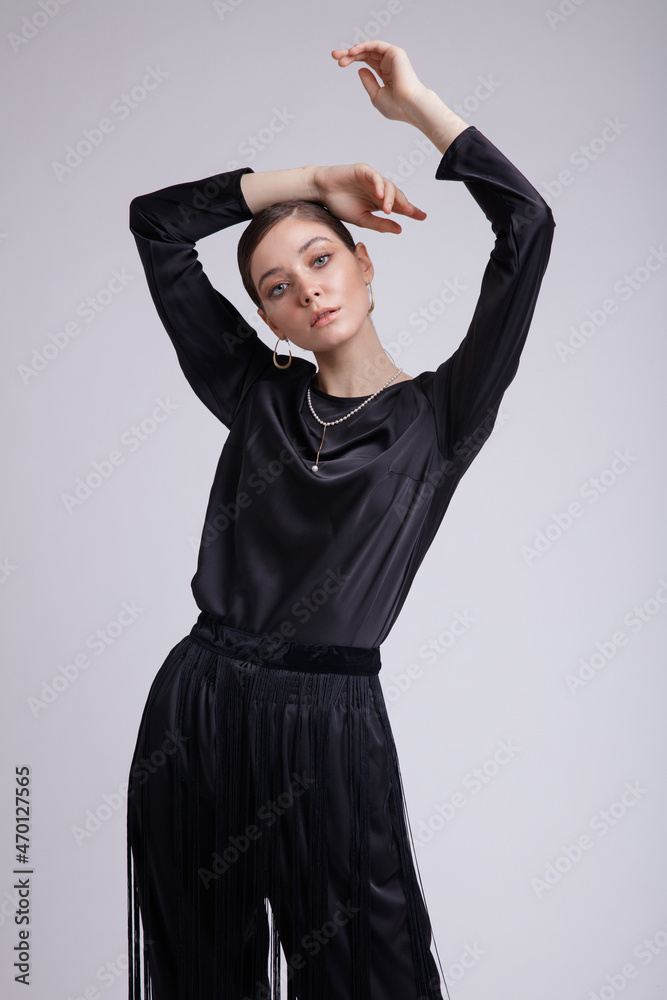 High fashion photo of a beautiful elegant young woman in a pretty black blouse, fringe trousers, accessories over white background. Studio Shot. Gathered dark hair. Slim figure