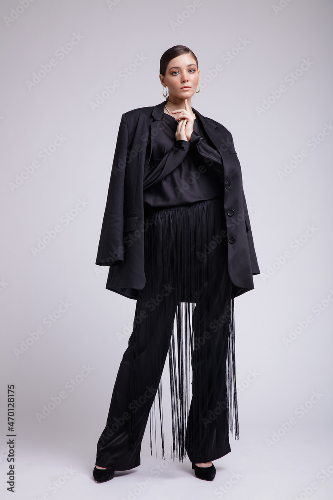 High fashion photo of a beautiful elegant young woman in a pretty black jacket, blouse, fringe trousers, accessories over gray background. Studio Shot. Gathered dark hair. Slim figure High fashion photo of a beautiful elegant young woman in a pretty black jacket, blouse, fringe trousers, accessories over gray background. Studio Shot. Gathered dark hair. Slim figure