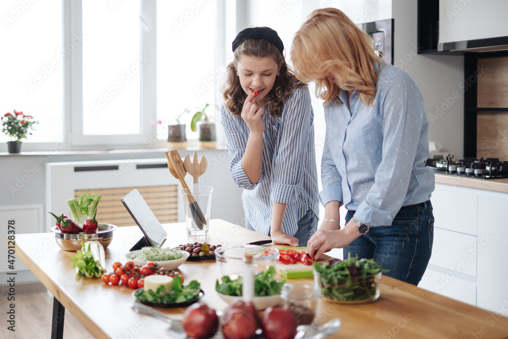 Mom and daughter cooking together in the kitchen. They use vegetables for cooking in a good mood, happy to be together