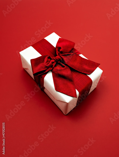 Fototapeta Naklejka Na Ścianę i Meble -  Gift box wrapped in white paper with red silk ribbon on red surface. Christmas and New Year luxury present, Valentine's day or birthday surprise concept. Angle view, copy space.