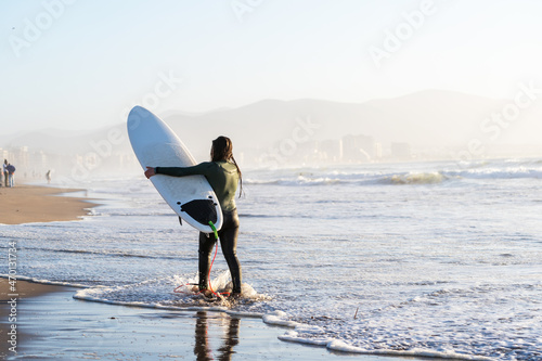 young female surfer walking on the beach holding surfboard in La Serena Chile 