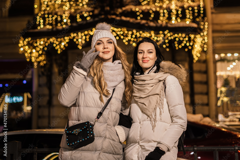 two beautiful young women in winter on a city street with blurry lights