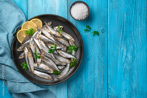 Sprat in a black plate with lemon and parsley on a blue background.