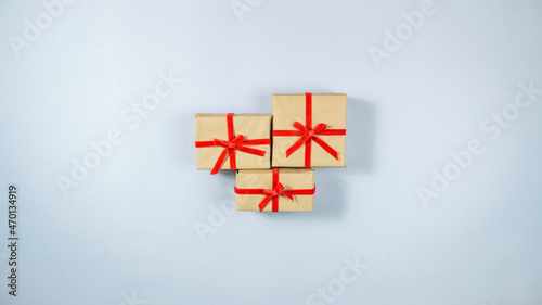 Three boxes wrapped in craft paper and tied with red ribbon in center on light gray background.