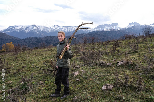 Teenager in green jacket with firewood in mountains. 