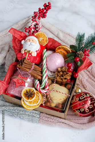 gift box with christmas decor, cookies, cinnamon, candies, beauty product and sweater on marble background. eco friendly gift idea for family and friends. festive winter season. Top view	