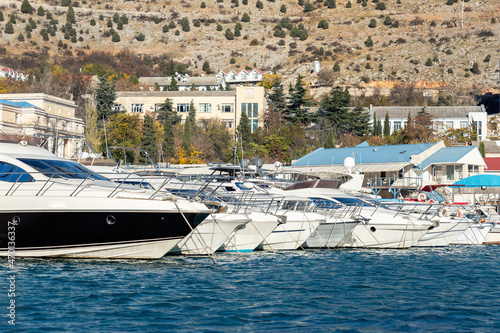 Scenic view of many luxury sailing fishing boat and charter rental speedboats moored at mountain harbor lake bay against mountain landscape backgound on sunny day. Sea marina vessel pier sorage dock photo