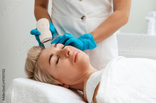 Professional care. A cosmetologist in blue gloves does an ultrasound cleaning of a woman s face. Cleansing and rejuvenating procedure in a beauty salon. Side view