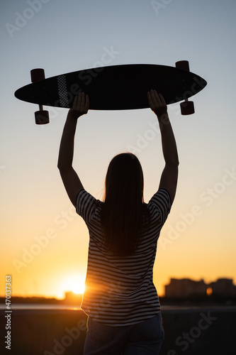 Canvas Freedom and urban fashion: teenage girl with longboard looking at sunset, evening sky on background