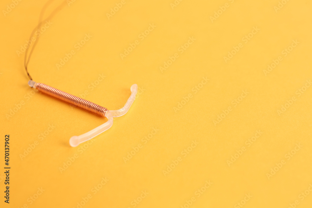 Copper intrauterine contraceptive device on yellow background. Space for text