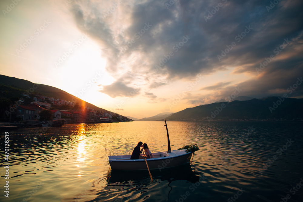 Man and woman kiss in a boat in the middle of the water against the backdrop of the sunset