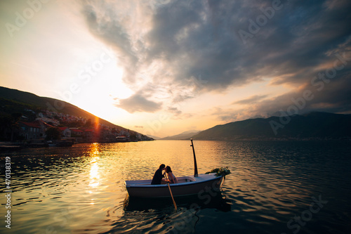 Man and woman kiss in a boat in the middle of the water against the backdrop of the sunset © Nadtochiy