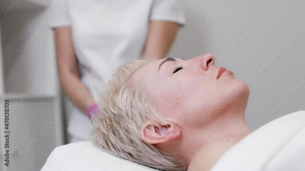 A client is undergoing a procedure at a beauty salon. A woman's face in close-up. In the background, the beautician puts on gloves. Slow motion. A client is undergoing a procedure at a beauty salon. A woman's face in close-up. In the background, the beautician puts on gloves. Slow motion.