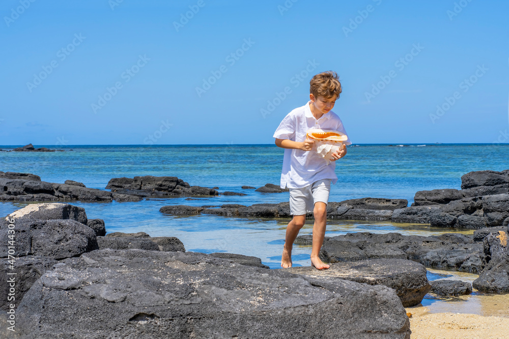 A boy walking with a big seashell in his hand on the tropical beach. High quality photo