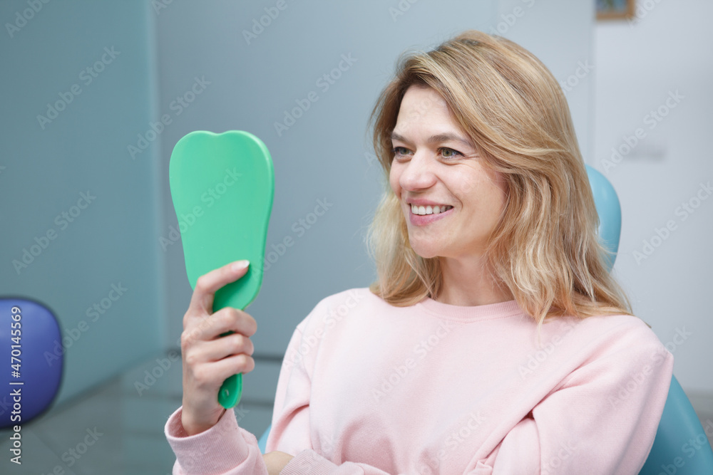 Happy mature woman smiling with her healthy white teeth to the mirror after dental treatment at the clinic Happy mature woman smiling with her healthy white teeth to the mirror after dental treatment at the clinic