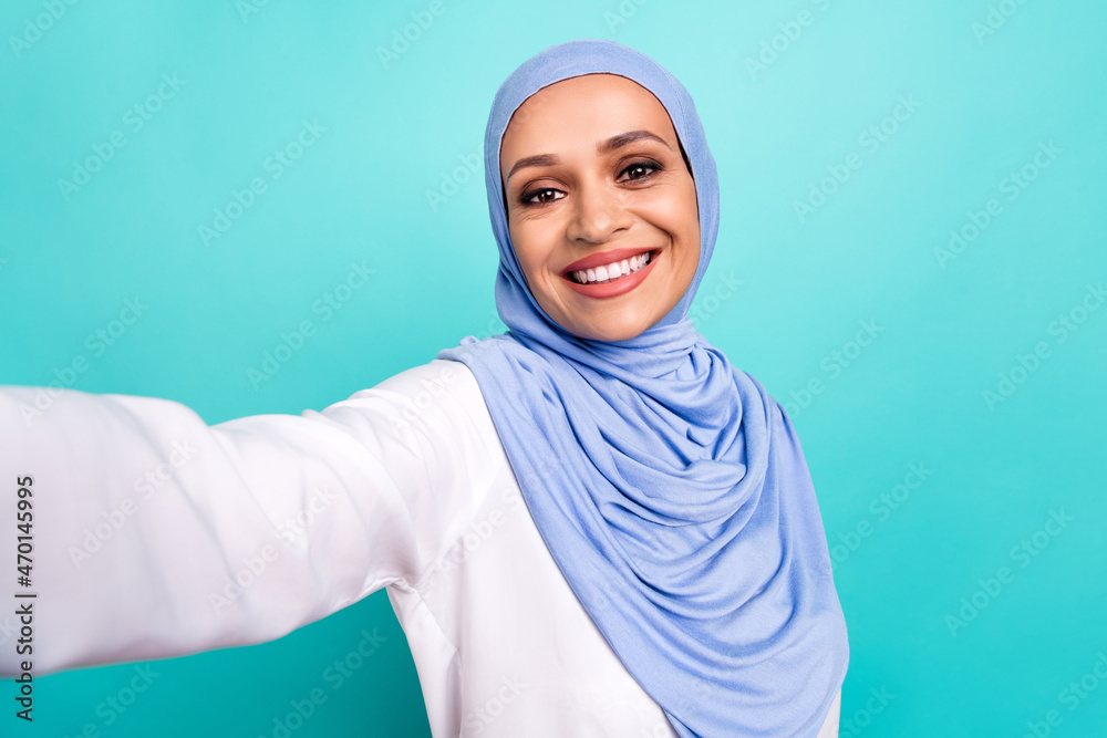 Photo of dreamy pretty young lady dressed islamic hijab smiling tacking selfie isolated teal color background Photo of dreamy pretty young lady dressed islamic hijab smiling tacking selfie isolated teal color background