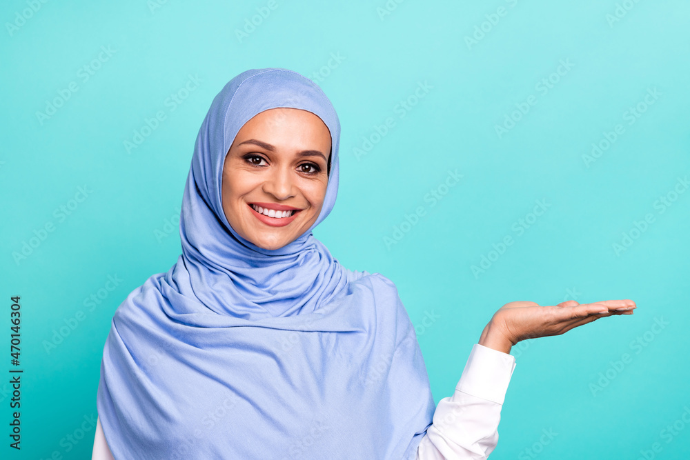 Photo of sweet charming young woman wear arab headscarf holding arm empty space smiling isolated turquoise color background Photo of sweet charming young woman wear arab headscarf holding arm empty space smiling isolated turquoise color background