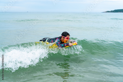 cute asian girl wearing a black swimsuit running on the waveboard surf in the sea on a bright day