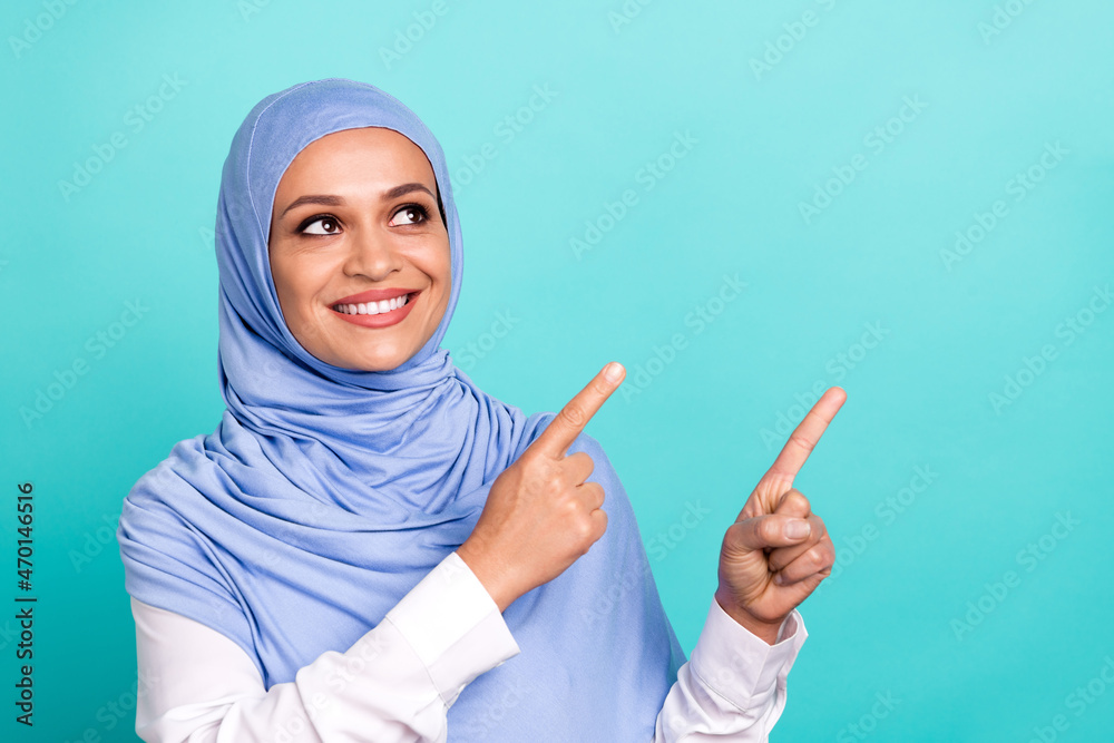Photo of charming pretty young lady dressed islamic hijab smiling pointing lookig empty space isolated teal color background Photo of charming pretty young lady dressed islamic hijab smiling pointing lookig empty space isolated teal color background