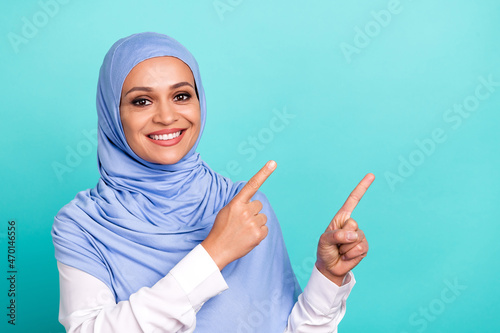 Photo of dreamy shiny young woman wear arab headscarf pointing fingers empty space smiling isolated turquoise color background