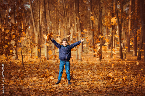 A boy in a blue jacket throws up leaves in an autumn park. Autumn park walk concept © popovatetiana