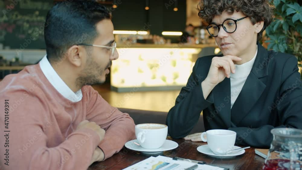 Ambitious businesswoman in elegant suit is talking to Middle Eastern partner in cafe discussing cooperation smiling. Business communication and lifestyle concept. Ambitious businesswoman in elegant suit is talking to Middle Eastern partner in cafe discussing cooperation smiling. Business communication and lifestyle concept.