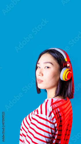 Confident asiatic woman indoors wearing wireless headphones looking camera confident and attitude enjoying streaming music positive - vertical copyspace cropped banner