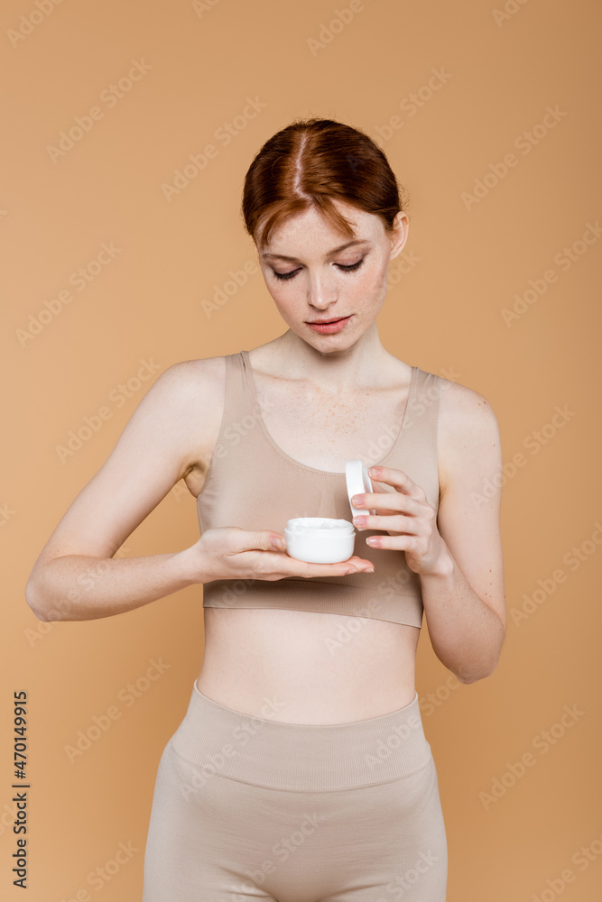Freckled woman in top looking at cosmetic cream isolated on beige Freckled woman in top looking at cosmetic cream isolated on beige
