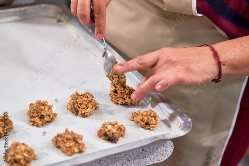 Woman places unbaked oatmeal cookies on steel tray.