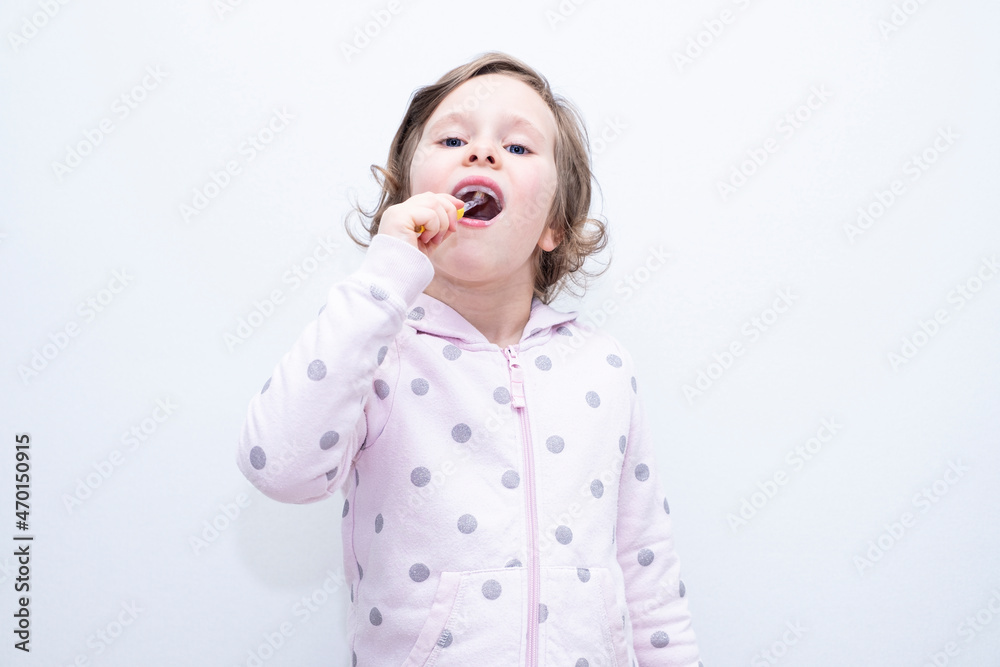 The child thoroughly brushes his teeth with a toothbrush and toothpaste. Hygiene of teeth and oral cavity. Caucasian girl on a gray background. The child thoroughly brushes his teeth with a toothbrush and toothpaste. Hygiene of teeth and oral cavity. Caucasian girl on a gray background.