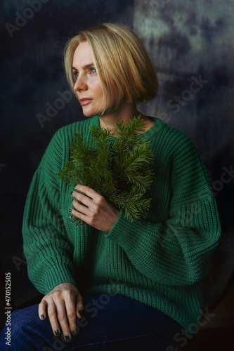 Portrait of a beautiful woman with a green sweater with fir branches in her hands.